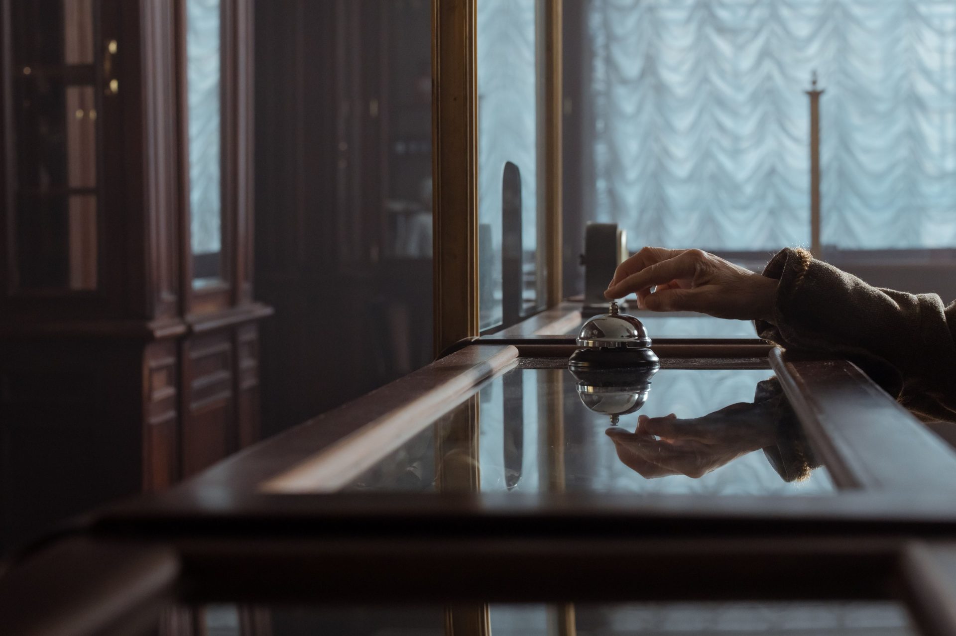 A hand pressing a service bell on an elegant wooden hotel desk, creating a classic atmosphere.