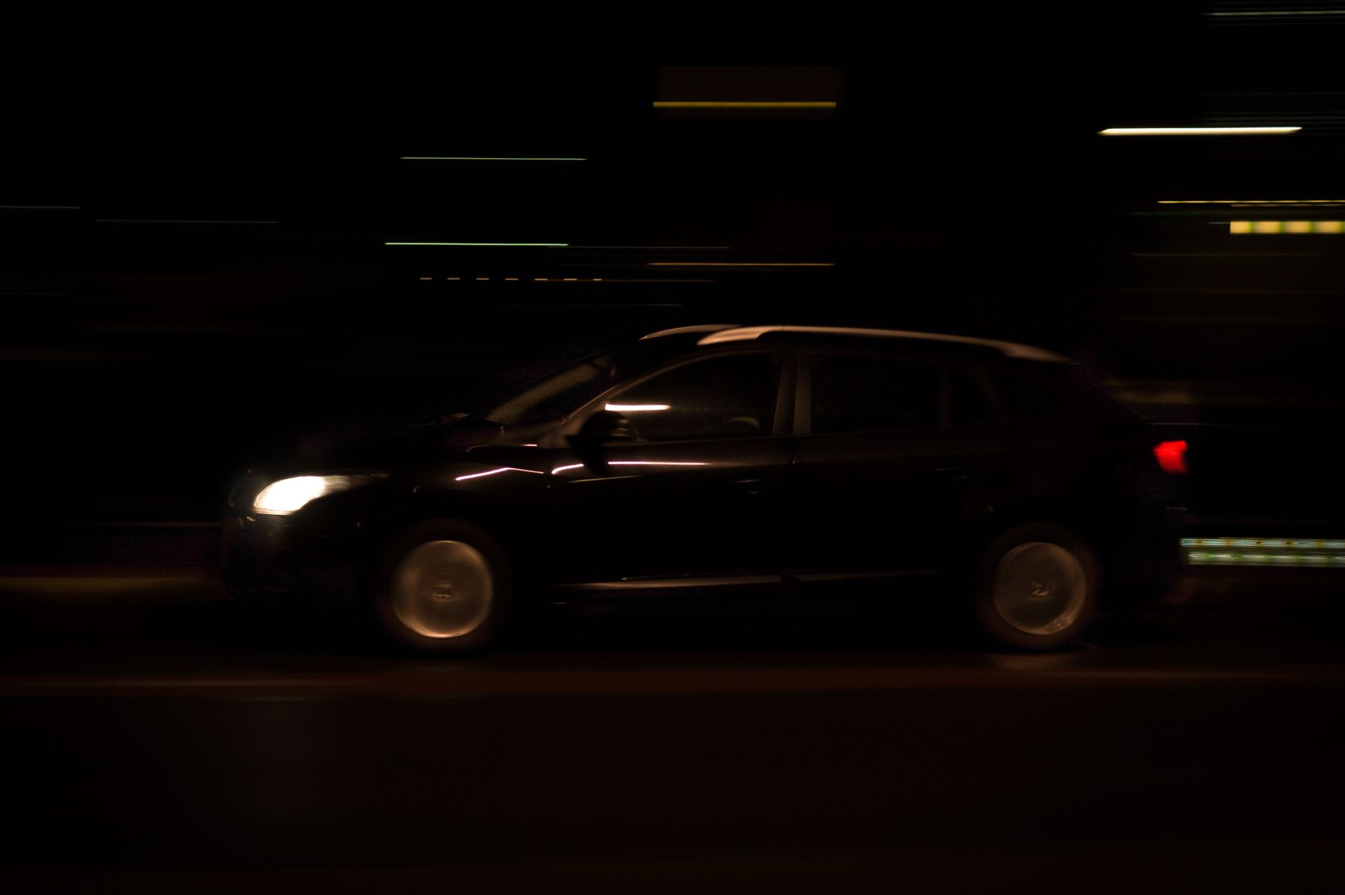 A sleek car speeds through a dimly lit urban tunnel at night, with headlights streaking in motion blur.
