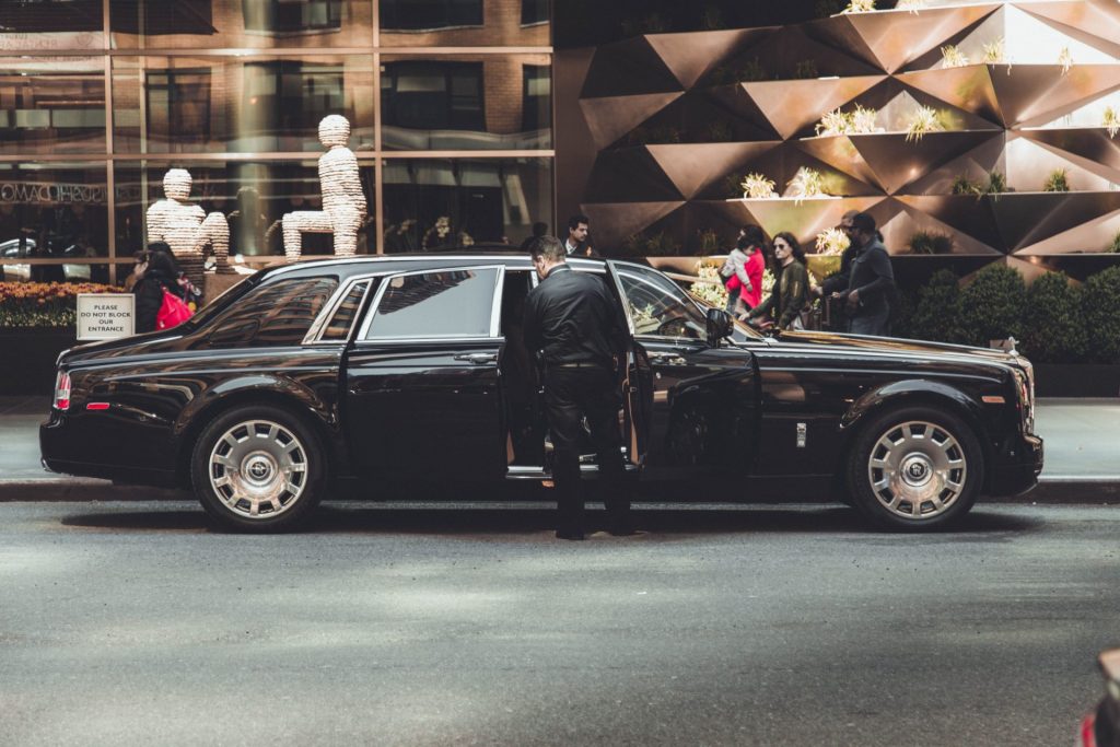 chauffeur-prive-ouvrant-la-portiere-dune-rolls-royce-phantom-noire-devant-un-etablissement-de-luxe-pour-accueillir-un-client